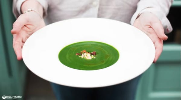 La cheffe présente une assiette de velouté vert devant la façade vert d'eau